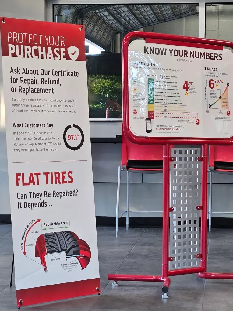Two informational signs in a tire service area. The left sign promotes a purchase protection certificate for tire repair, refund, or replacement, highlighting customer satisfaction rates. The right sign explains tire depth and age, detailing how these factors impact tire performance and safety.