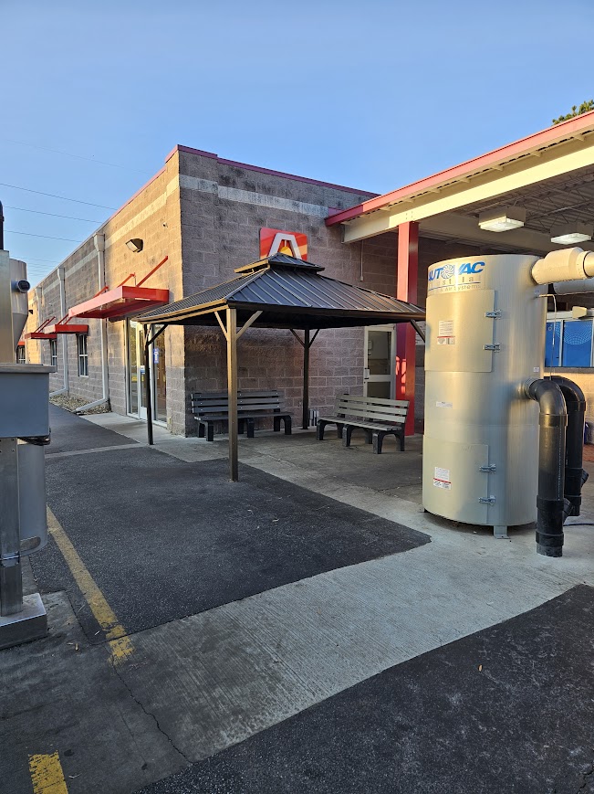 Exterior view of a building with a covered seating area, featuring benches and an adjacent industrial-looking tank.